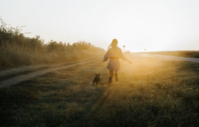 Rear view full length of young woman running with dog on land