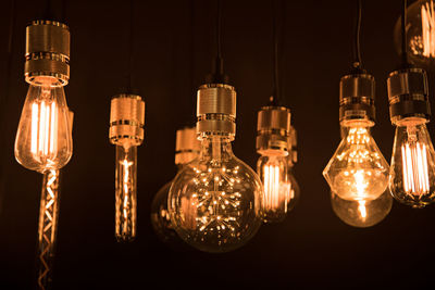 Close-up of illuminated light bulb hanging against black background