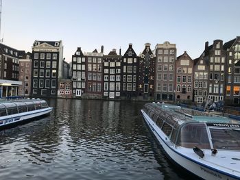 Boats moored in canal by buildings against clear sky