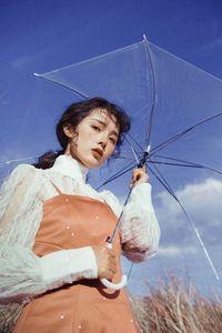 Young woman holding umbrella while standing on land against blue sky