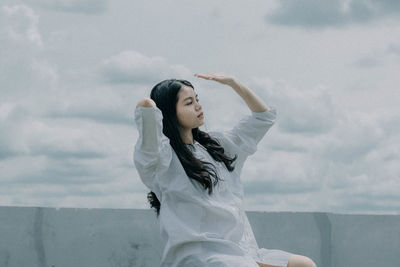 Young woman looking away against sky