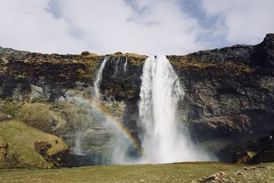 Scenic view of waterfall against cloudy sky