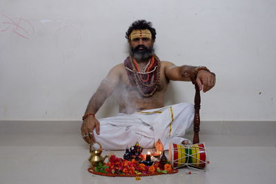 Full length portrait of young man sitting against wall