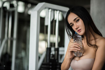 Portrait of young woman holding water bottle while standing in gym