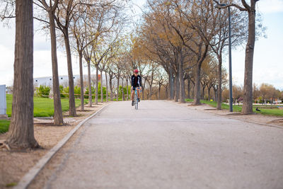 Male athlete cycling on road amidst bare trees against sky