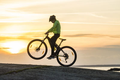 Boy cycling on beach at sunset