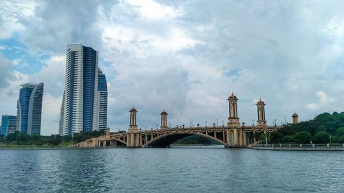 Bridge over river by buildings against sky