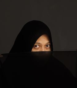 Portrait of woman wearing hijab against black background