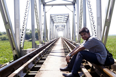 Man sitting on railroad track against sky