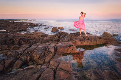 Beautiful young female model in pink dress standing on the rocky coast of wild atlantic way 