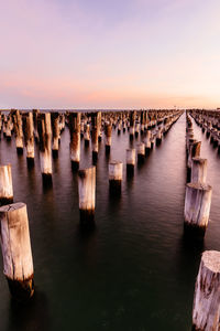 Wooden posts in sea against sky during sunset