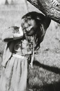 Portrait of smiling young woman holding tree trunk on field