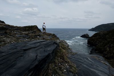 Rear view man standing on rock by sea against sky