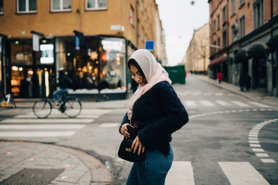 Side view of teenage girl removing mobile phone from purse while walking on street in city