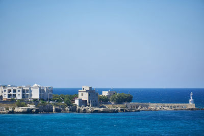 Buildings by sea against clear blue sky