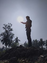 Optical illusion of man holding sun while standing on rock against sky