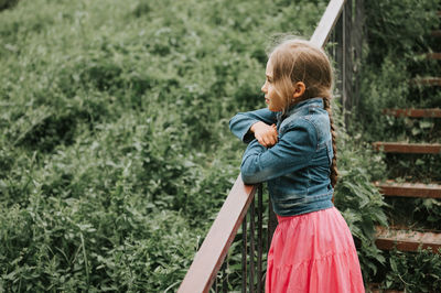 Thoughtful candid eight year old kid girl stands on staircase with grass and enjoying