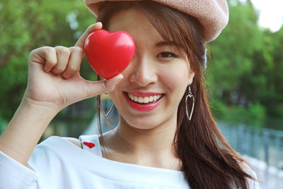 Close-up portrait of happy young woman holding heart shape on bridge