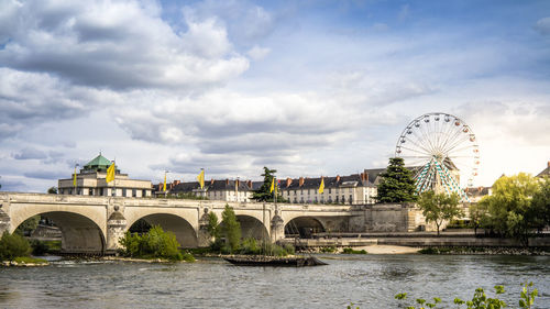 Bridge over river in city against cloudy sky