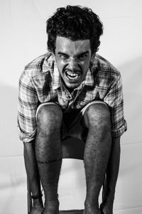 Portrait of angry man screaming while sitting on chair against white background