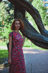 Portrait of young woman standing on tree trunk