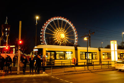 People at illuminated amusement park against sky at night