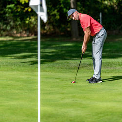 Golfer in the red shirt on the green, putting towards the golf flag