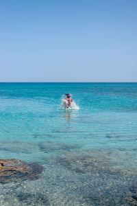 Rear view of woman swimming in sea against clear sky