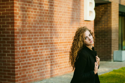 Portrait of woman sitting against brick wall