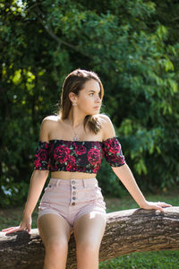 Thoughtful teenage girl looking away while sitting against trees in park