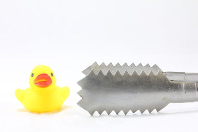 Close-up of rubber duck with serving tongs against white background