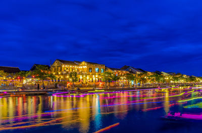 Illuminated buildings by sea against sky at night