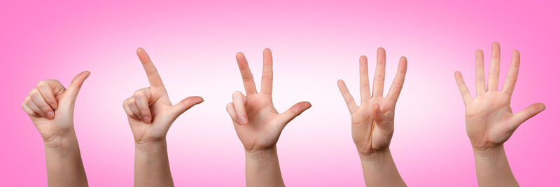 Cropped hands of person making signs against pink background