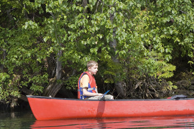 Side view of teenage boy wearing life jacket canoeing on lake