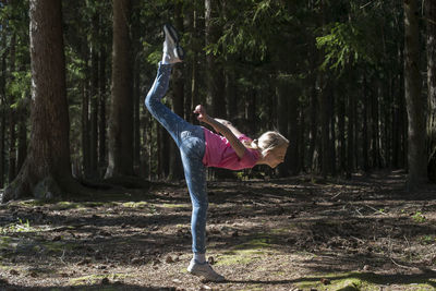 Side view of woman climbing on tree trunk in forest