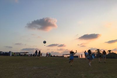 People playing with ball on field against sky during sunset