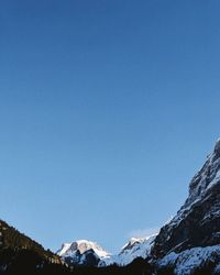 Low angle view of snowcapped mountains against clear blue sky