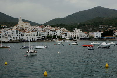 Sailboats moored on sea by buildings in city against sky