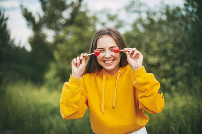 Smiling girl holding lollipops while standing against plants in park