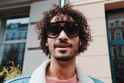 Portrait of smiling young man wearing sunglasses standing against house