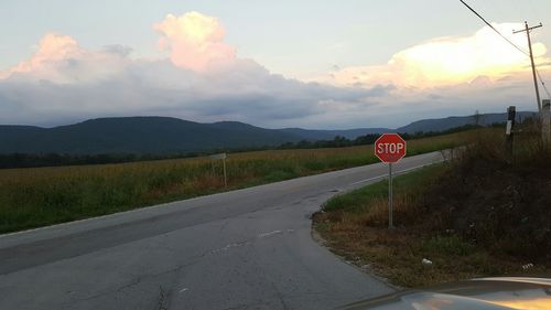 Road passing through field against cloudy sky