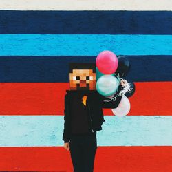 Person with pixelated face holding balloons against striped wall