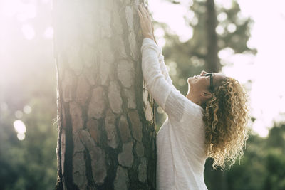 Side view of young woman standing against trees