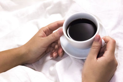 Midsection of woman holding coffee cup on bed