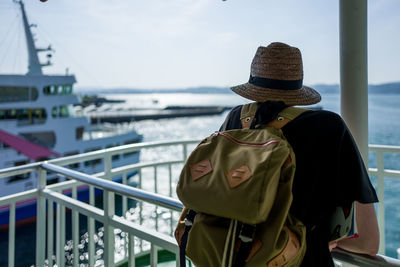 Rear view of man standing by railing on ferry while looking at boat in sea against sky