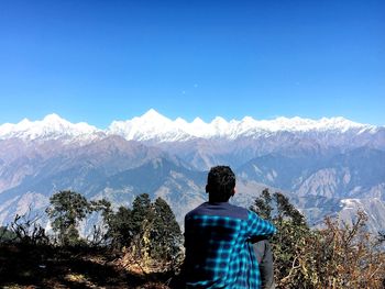 Rear view of person standing on mountain against blue sky