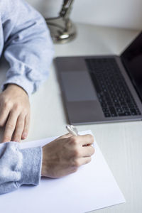 Midsection of person writing on paper sitting by table