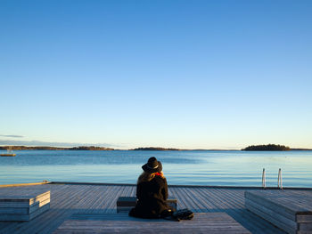 Rear view of woman sitting on pier against clear sky