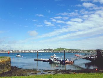 Boats moored at harbor against blue sky