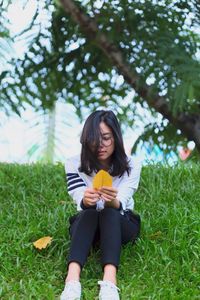 Mid adult woman holding leaf while sitting on grass